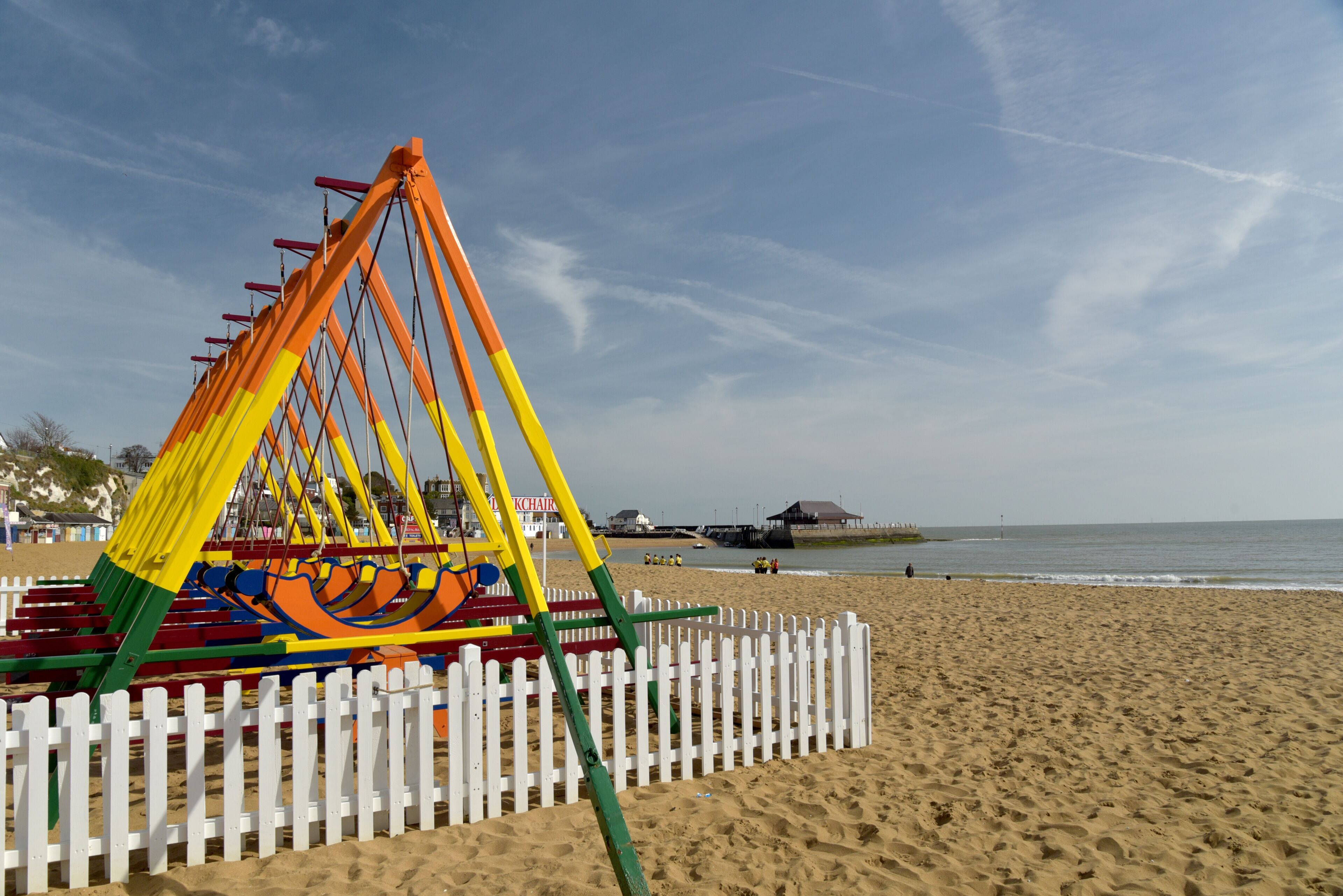 A beach with a colorful swing set and a white picket fence.