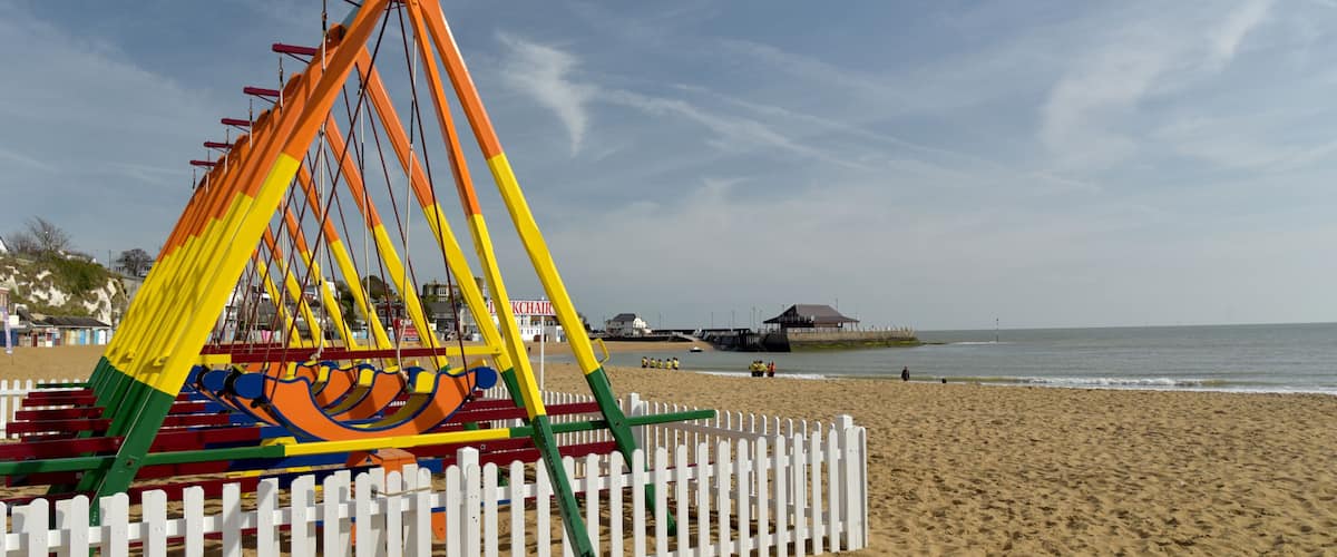 A beach with a colorful swing set and a white picket fence.