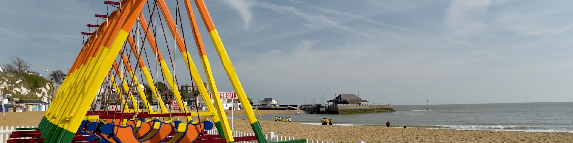 A beach with a colorful swing set and a white picket fence.