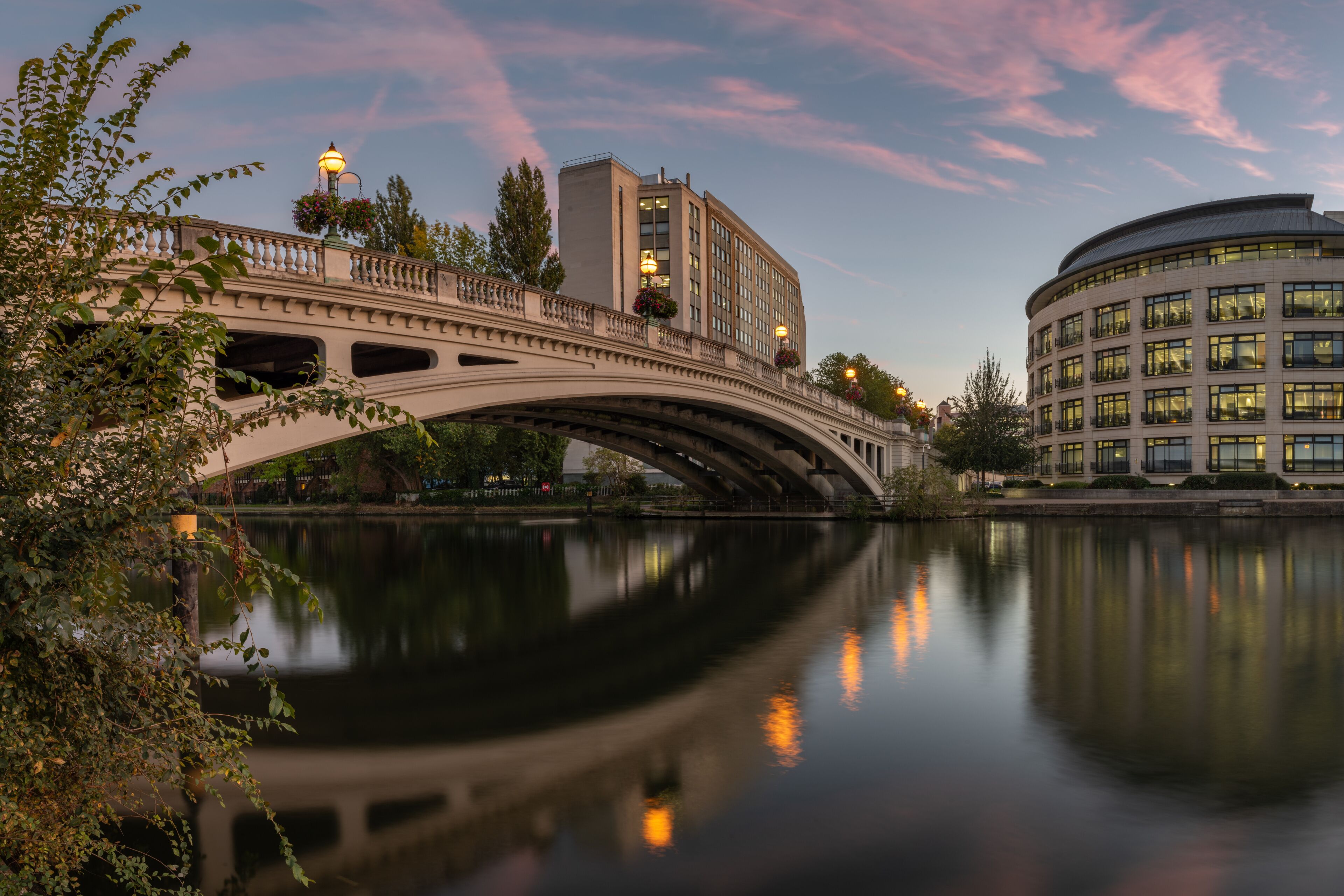 A bridge over a calm river, reflecting the surrounding buildings and sky.