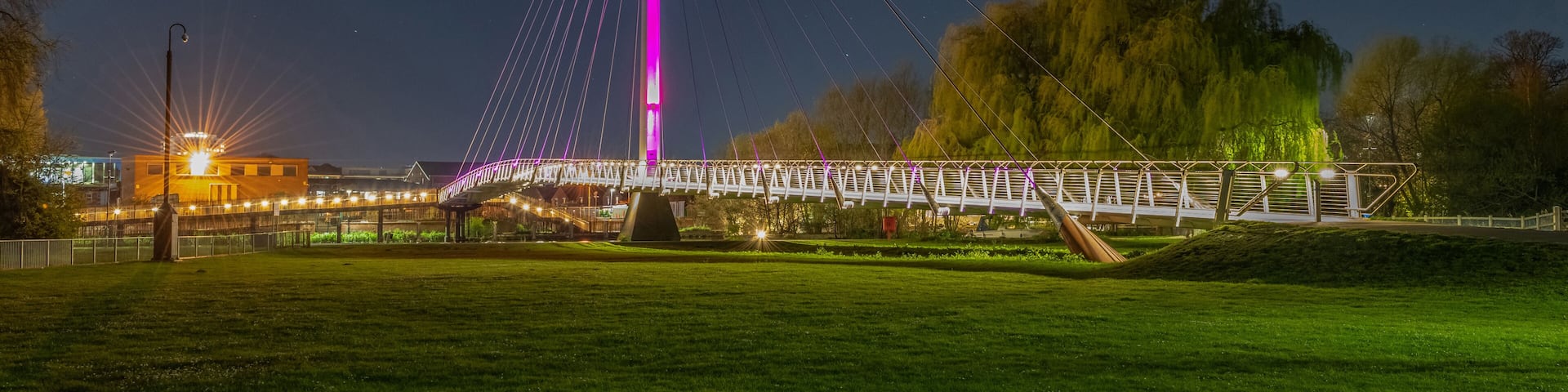 A bridge with a tall central tower, a crescent moon, and a park with grass and trees.