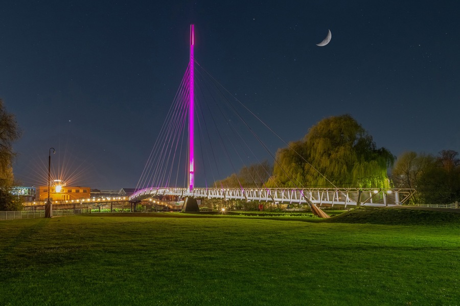 Un puente con una alta torre central, una luna creciente y un parque con césped y árboles.