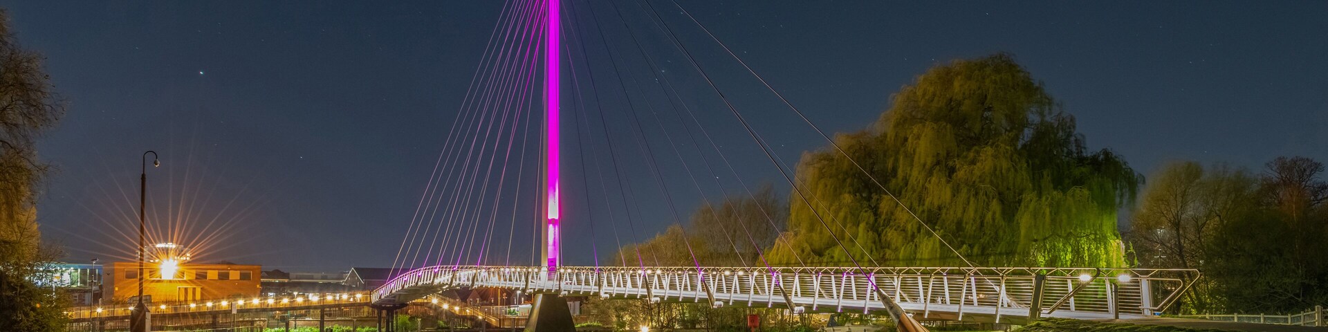 A bridge with a tall central tower, a crescent moon, and a park with grass and trees.