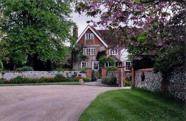 A traditional brick house with a stone wall, a gravel driveway, and flowering trees.