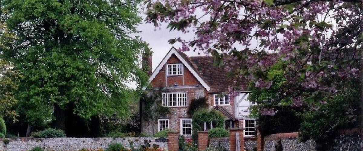 A traditional brick house with a stone wall, a gravel driveway, and flowering trees.
