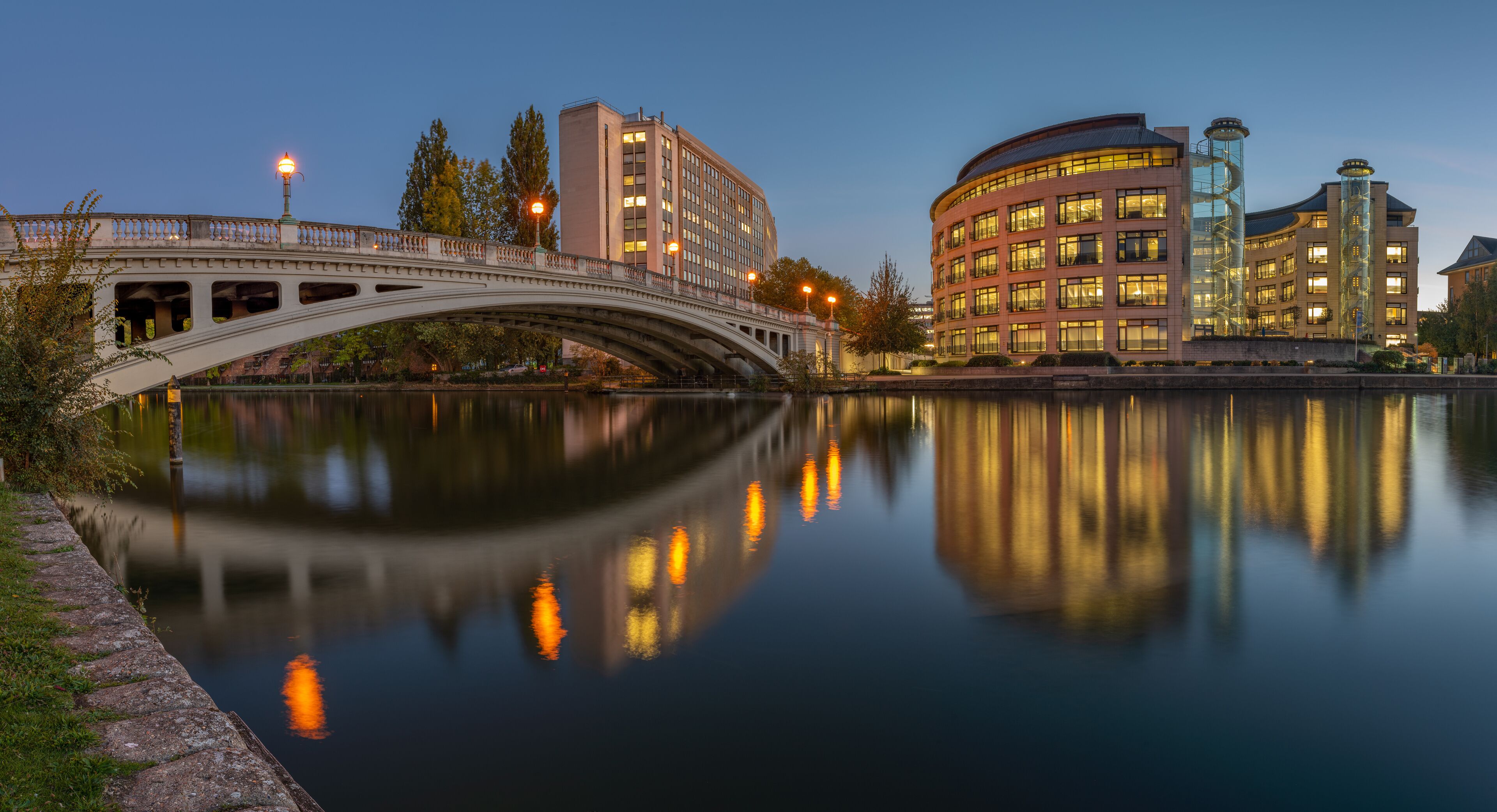 A bridge over a calm river, reflecting buildings and trees.