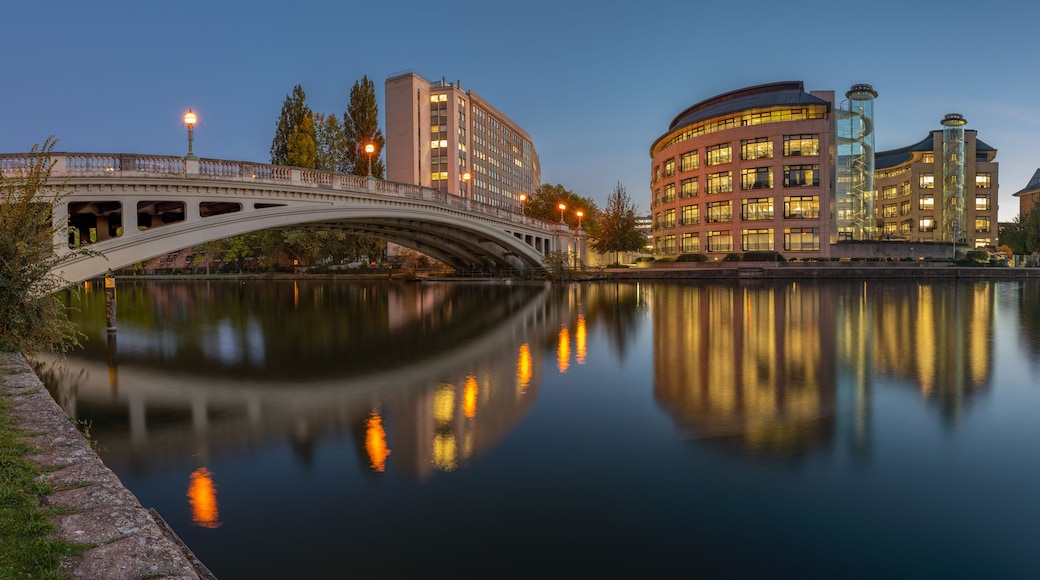 A bridge over a calm river, reflecting buildings and trees.