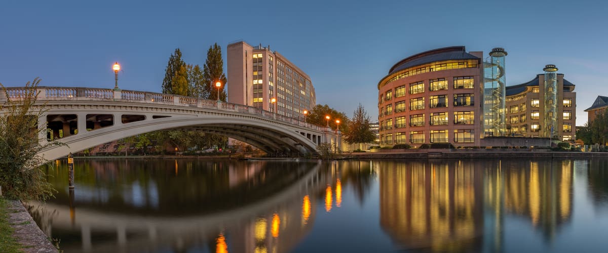 A bridge over a calm river, reflecting buildings and trees.