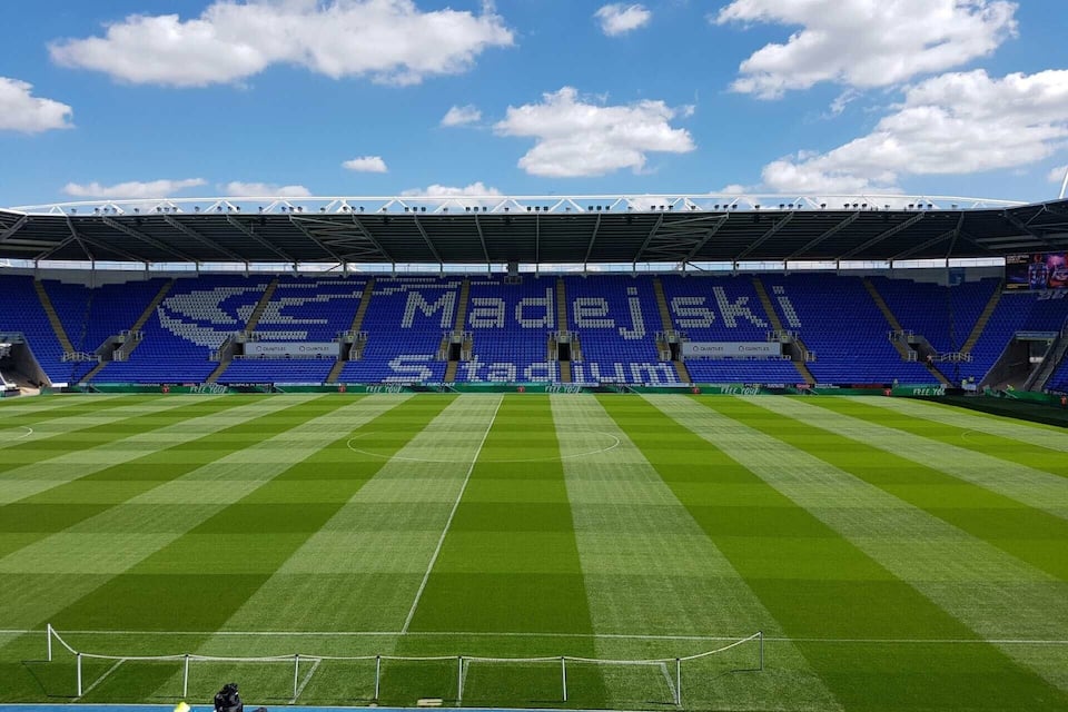 Un stade de football avec des sièges bleus et une grande publicité pour MADELEJKI.