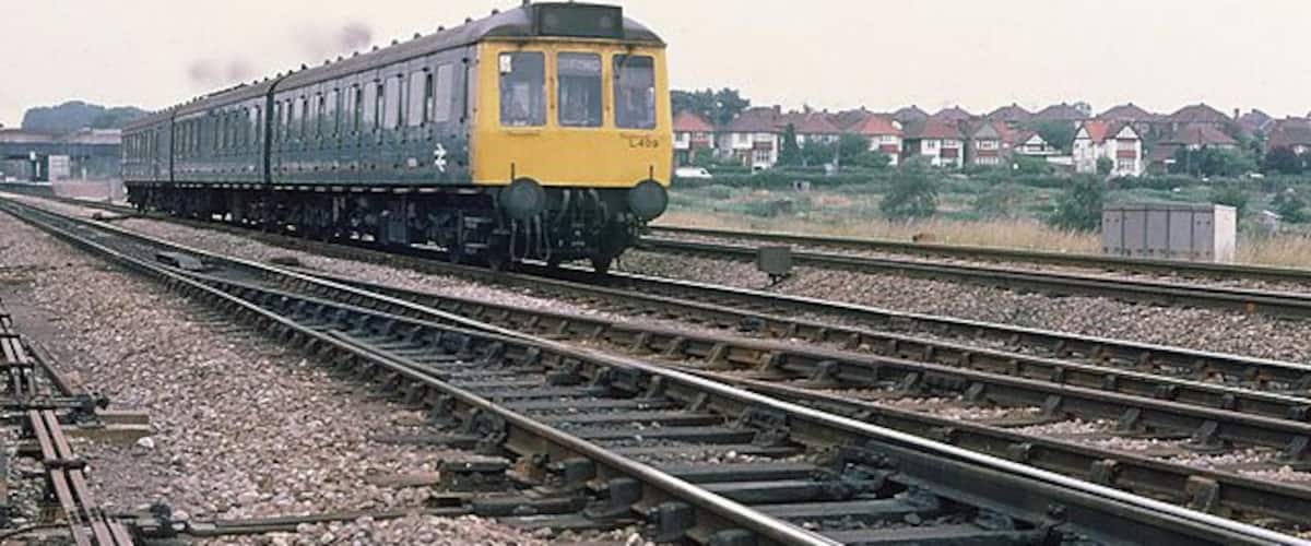 A yellow train on tracks with houses in the background.