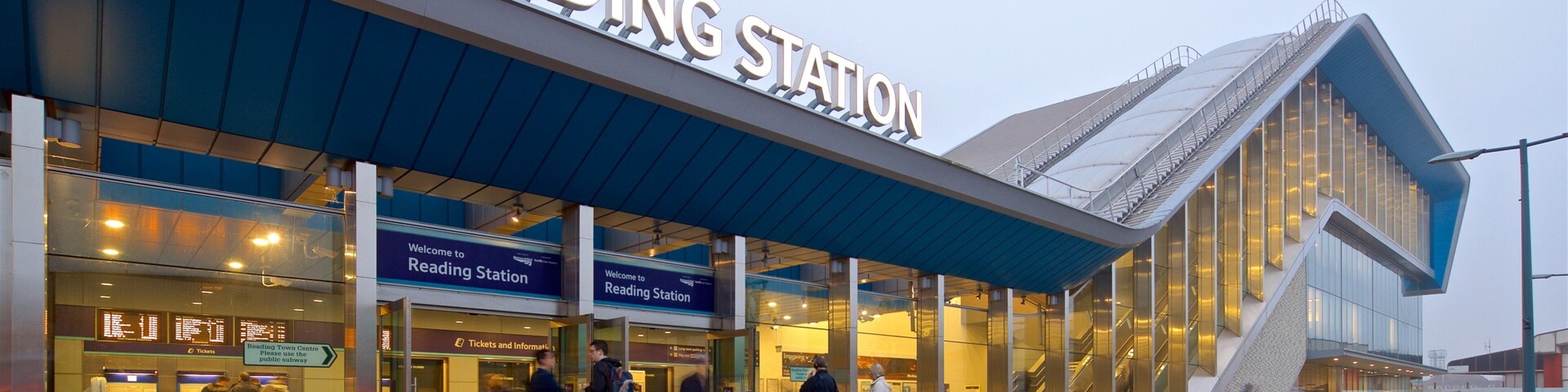 Estación de lectura con diseño moderno, que incluye un cartel grande, mostradores de venta de billetes y una entrada cubierta.