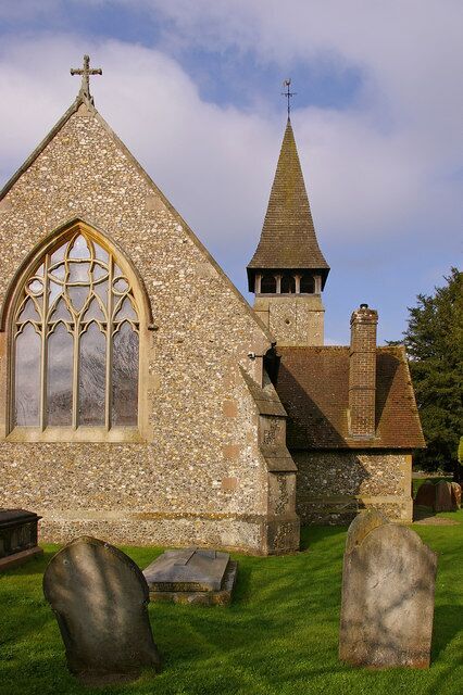 A church with a tall steeple, a large arched window, and a stone cross.