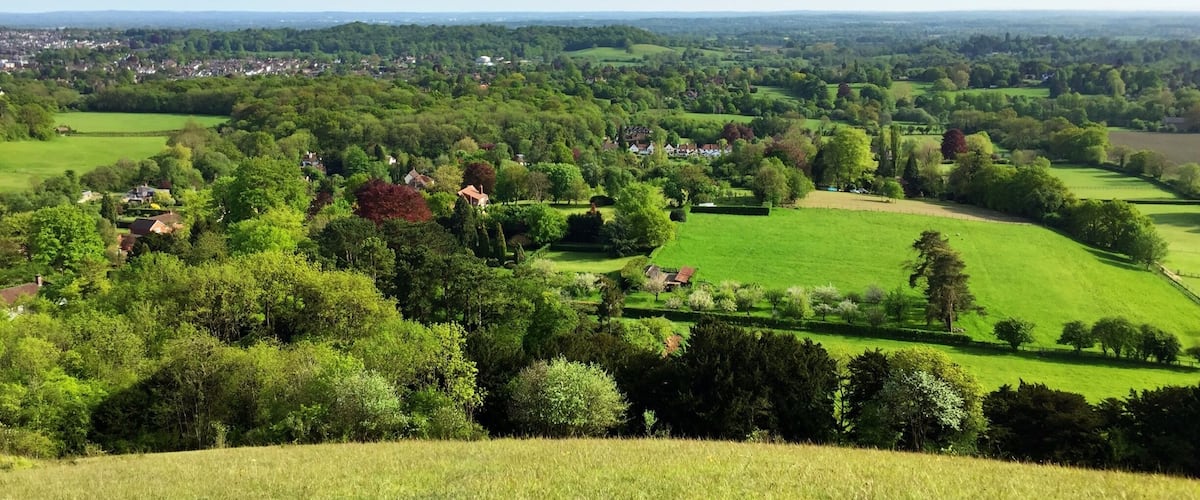 A lush green landscape with rolling hills, scattered houses, and a distant town.