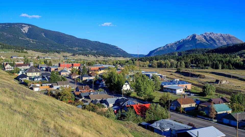 A small town nestled in a valley with houses, a road, and mountains in the background.