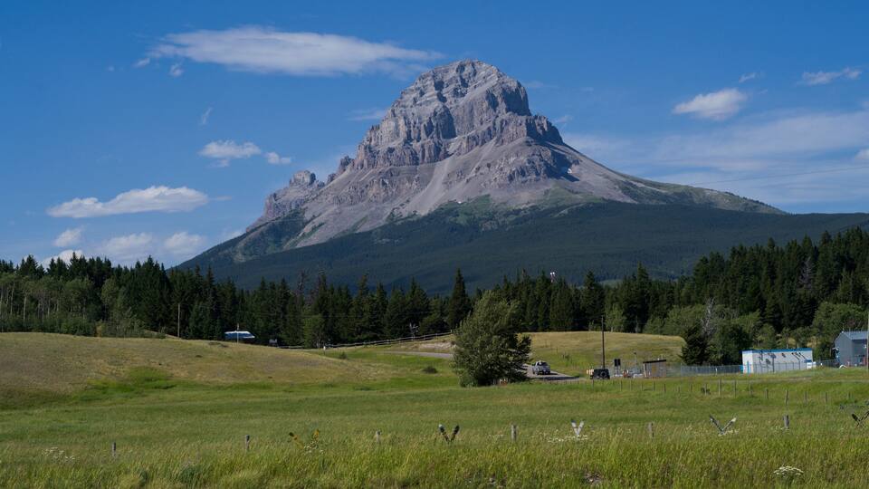 A mountain with a peak, surrounded by a forest and a small building.