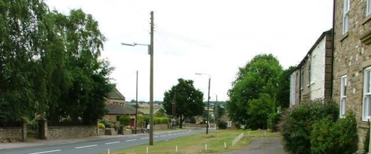 A residential street with houses, a grassy area, and a sidewalk.