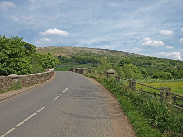 A rural road curving through a green landscape with stone walls and a wooden fence.
