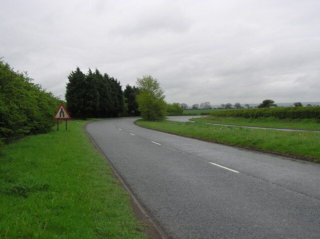 A rural road curving through a green landscape with a triangular warning sign.