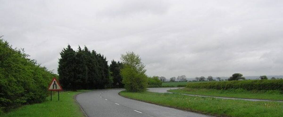 A rural road curving through a green landscape with a triangular warning sign.