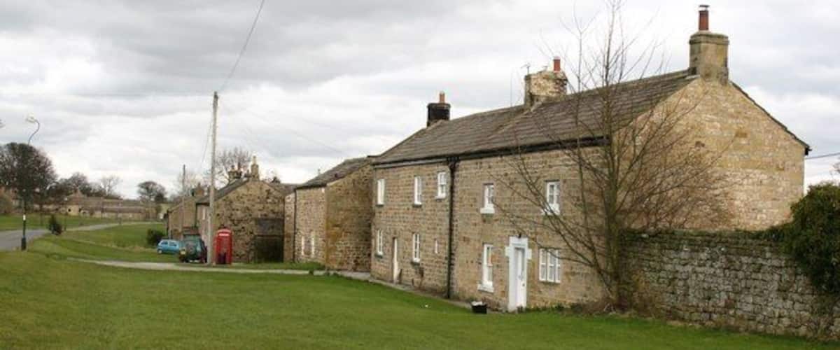 A stone house with a red door, a blue car, and a red telephone booth in a grassy area.