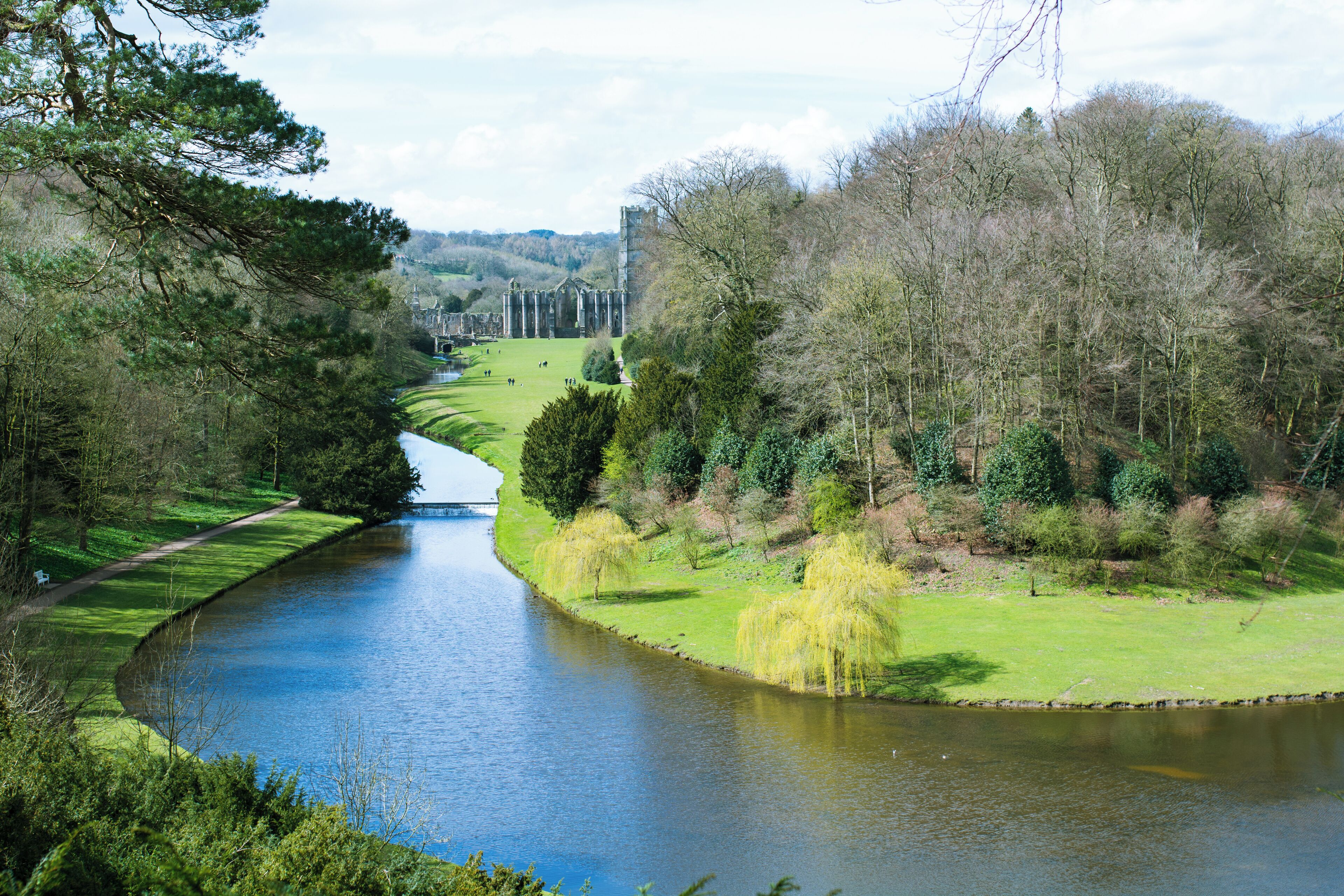 Un río serpentea por un parque con árboles y un castillo lejano.
