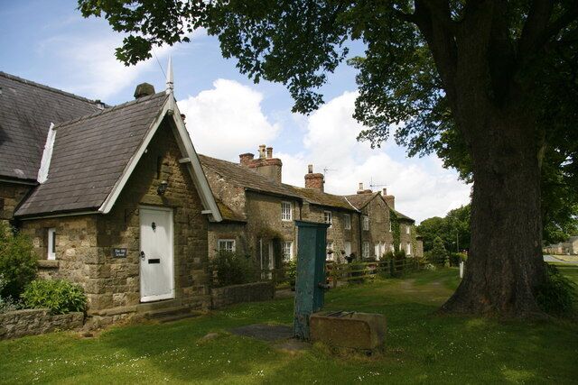 A stone house with a white door and a green door, surrounded by a grassy area and a large tree.