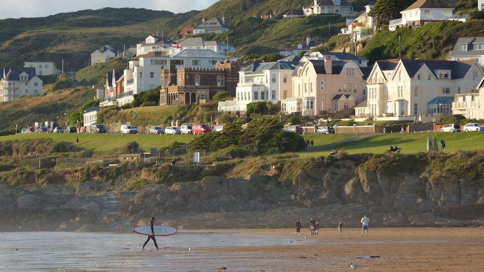 A beach with people, a surfer, and houses on a hillside.