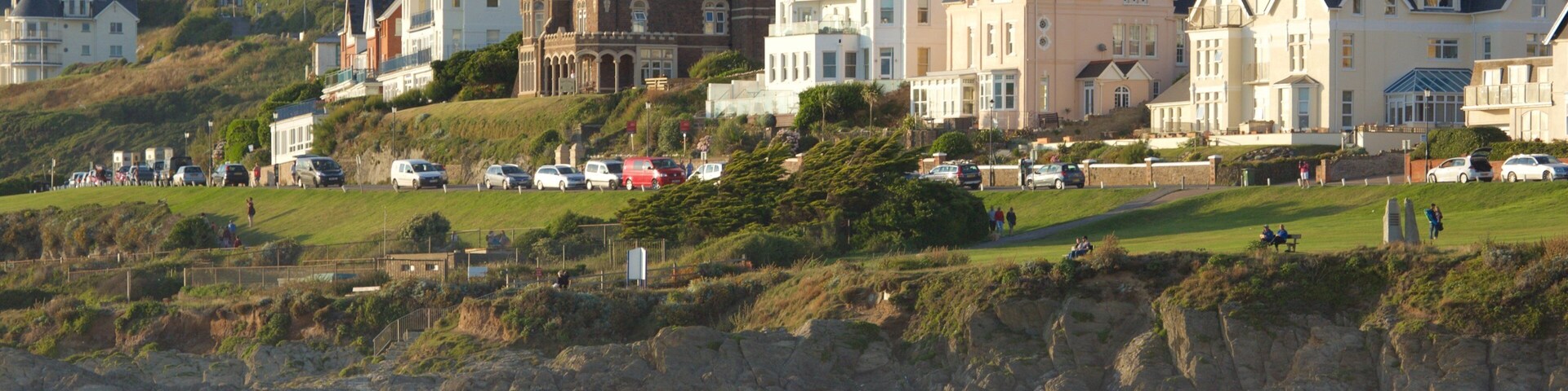 A beach with people, a surfer, and houses on a hillside.