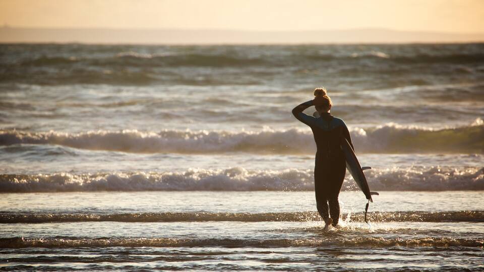 A surfer standing in the ocean with waves crashing around them.