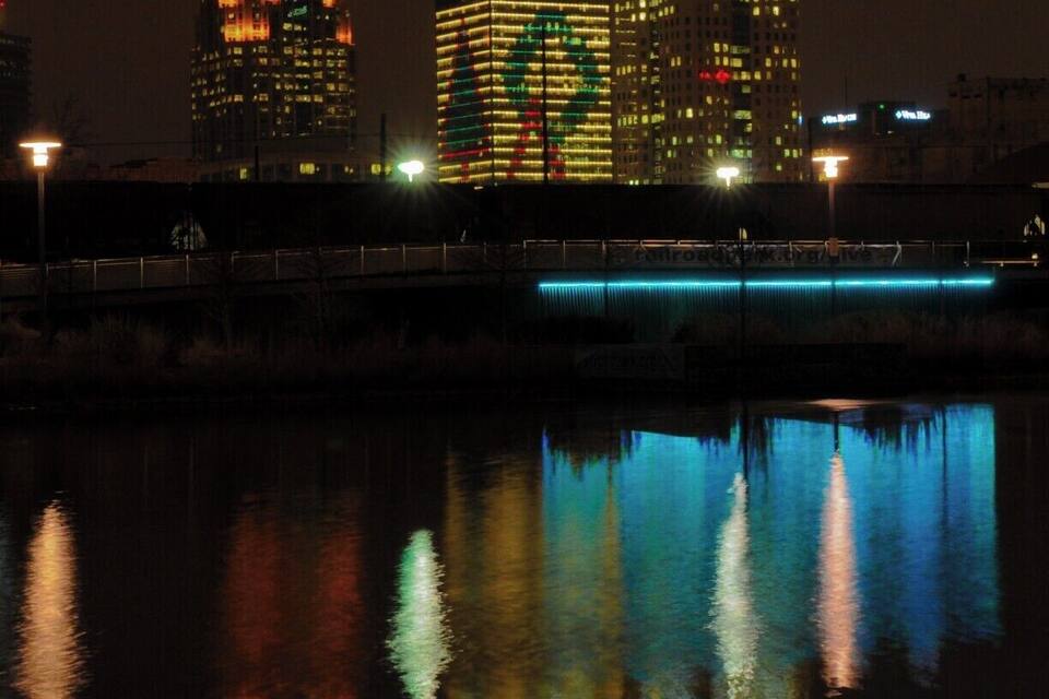 Een verlicht stadsbeeld 's nachts, met gebouwen die hun licht weerspiegelen in een kalm waterlichaam.