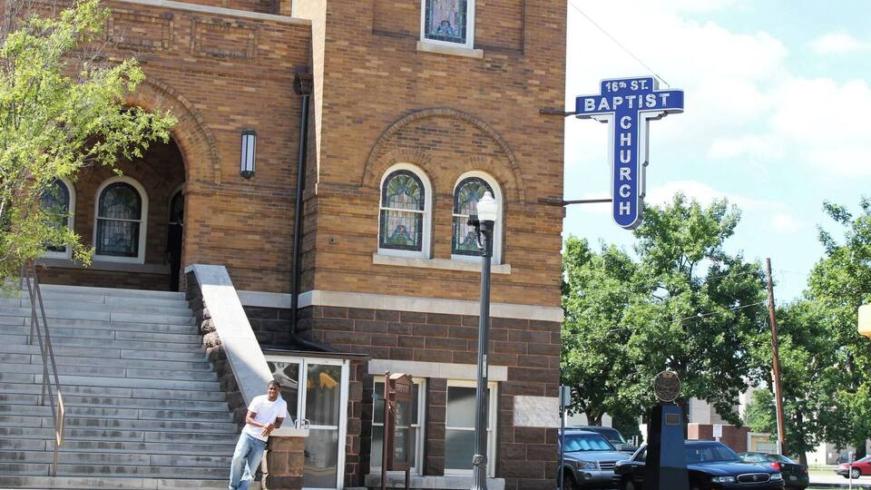 A brick building with a stained glass window and a street sign reading "16th St. Baptist Church".