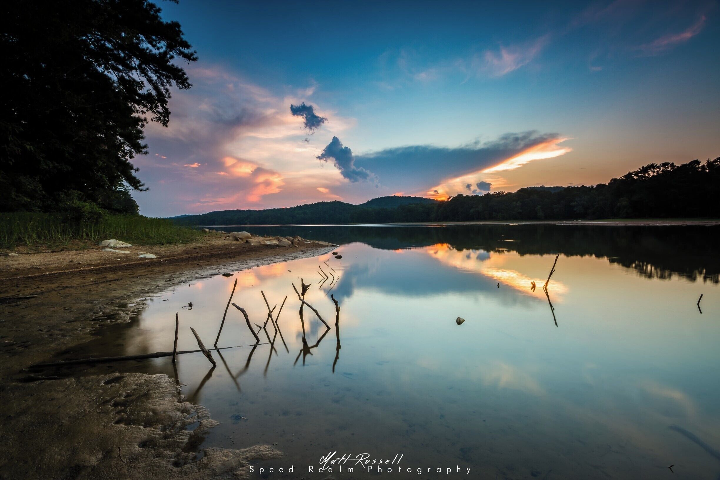 Um lago calmo ao pôr do sol, refletindo árvores e o céu.