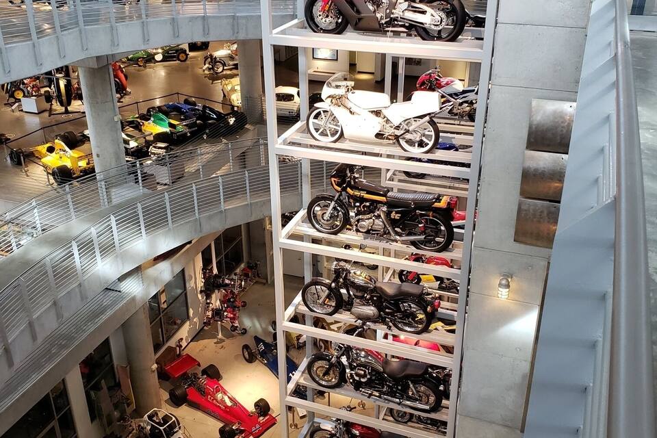 Een meerlaagse overdekte showroom voor motoren, met diverse modellen op planken tentoongesteld.