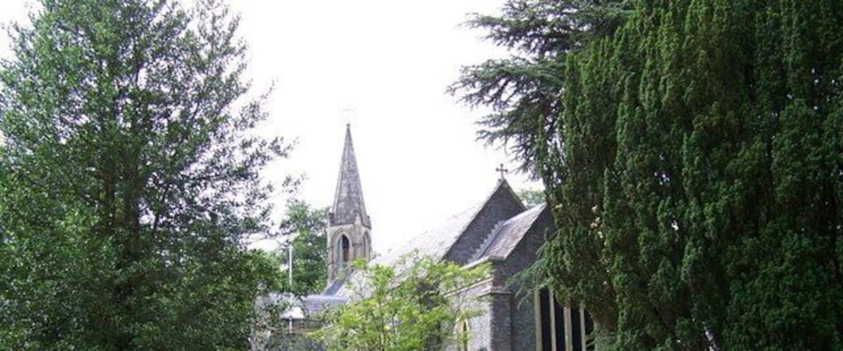 A church with a tall steeple, surrounded by trees and gravestones.