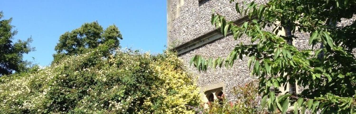A historic stone building with a tower, surrounded by lush greenery and flowering plants.