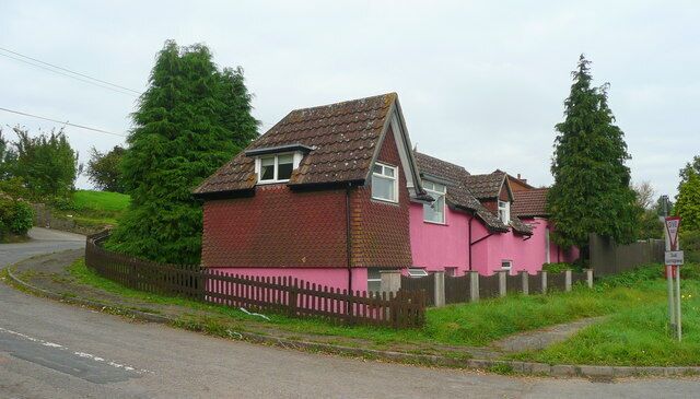 A pink house with a brown roof, surrounded by a fence and trees.