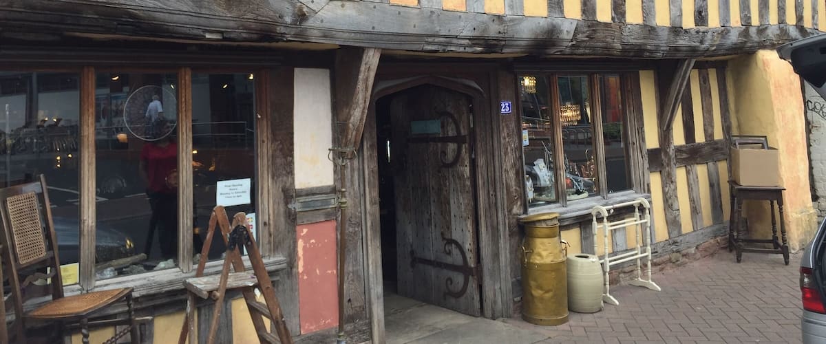 A half-timbered building with a yellow and black facade, a wooden door, and a sign indicating it is a restaurant.