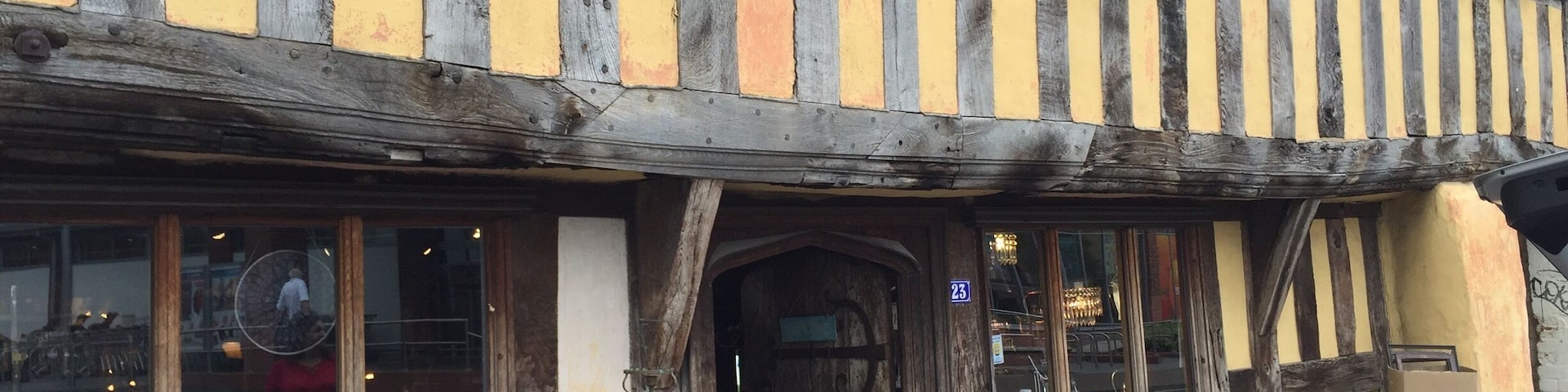 A half-timbered building with a yellow and black facade, a wooden door, and a sign indicating it is a restaurant.