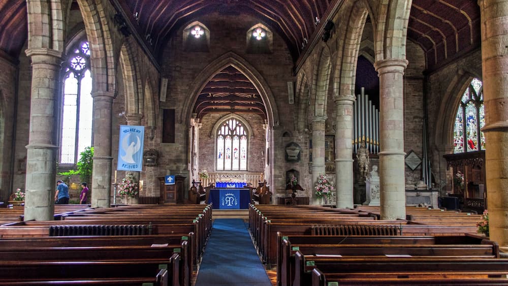 L’intérieur d’une église, avec des voûtes en arc, des bancs en bois, des vitraux et une allée centrale menant à l’autel.