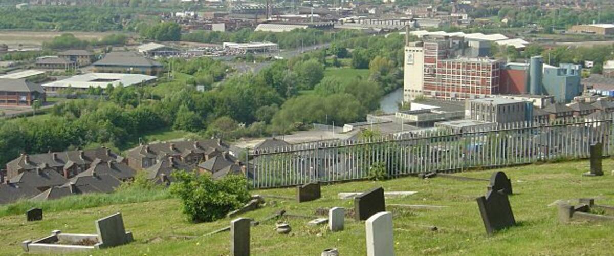 A cemetery with headstones, a fence, and buildings in the background.