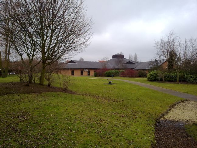 A building with a sloped roof, surrounded by a grassy area with a path leading to it.