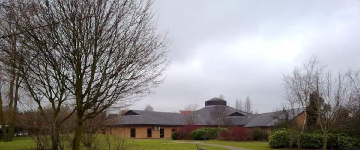 A building with a sloped roof, surrounded by a grassy area with a path leading to it.