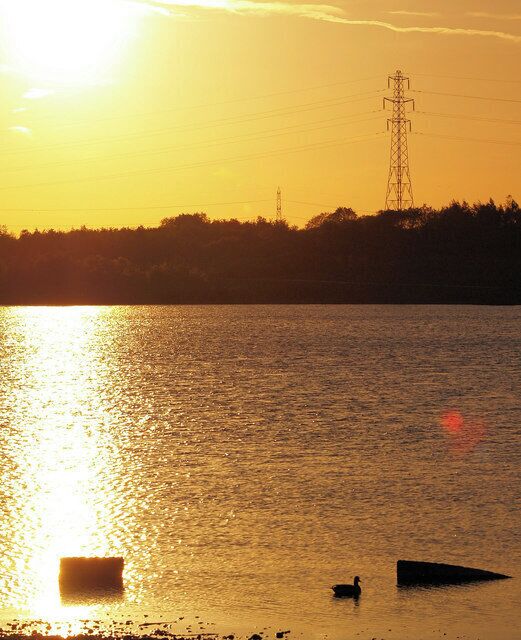 Um pôr do sol sobre a água, com uma torre de linhas de energia ao fundo.