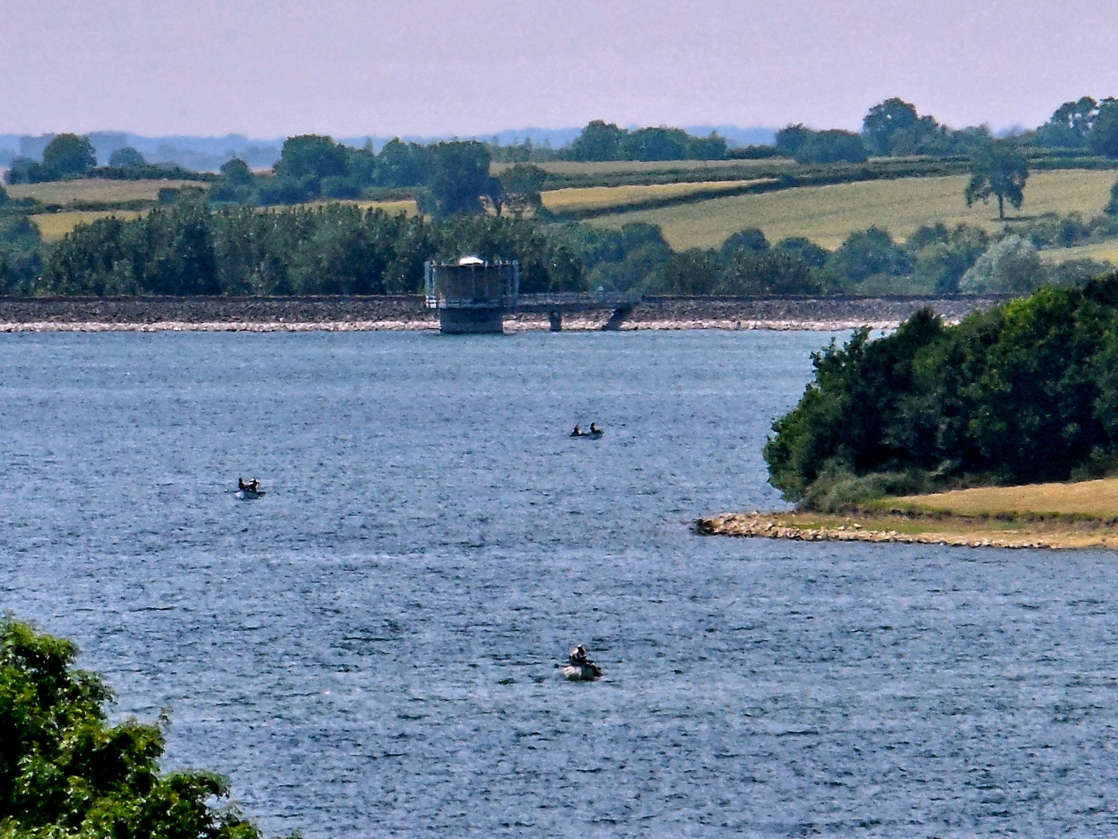 A calm lake with a small island and a bridge in the distance.