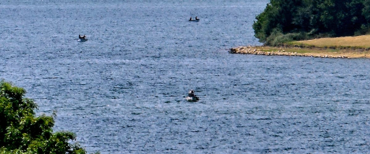 A calm lake with a small island and a bridge in the distance.