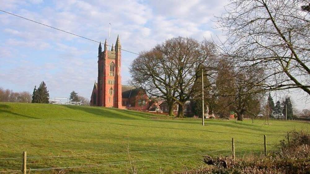 A church with a tall tower, a green field, and leafless trees.