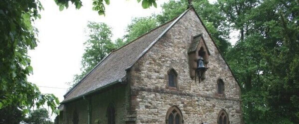 A stone church with a bell tower, surrounded by greenery.