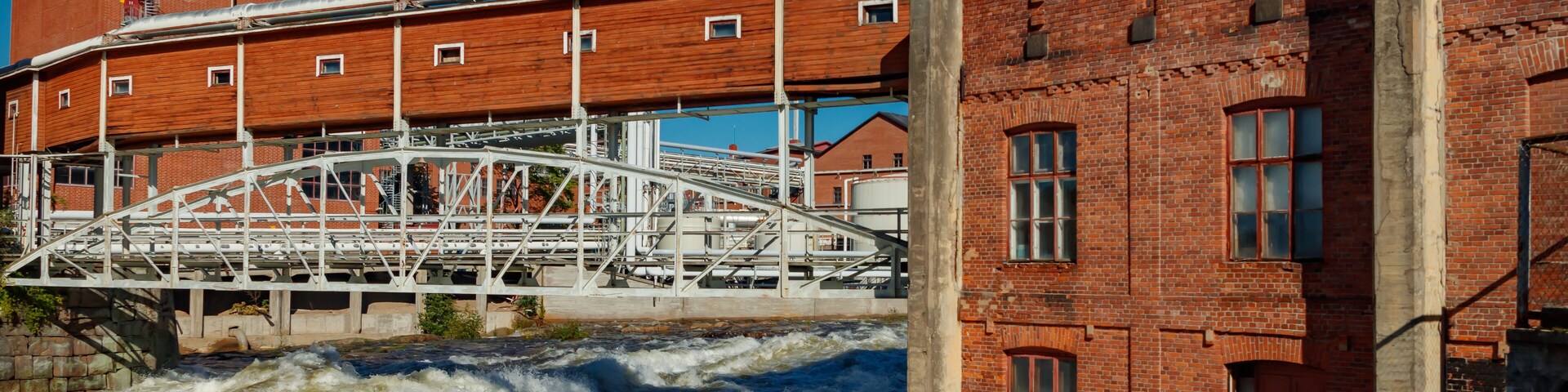 A river with a bridge, a brick building, and a metal structure.
