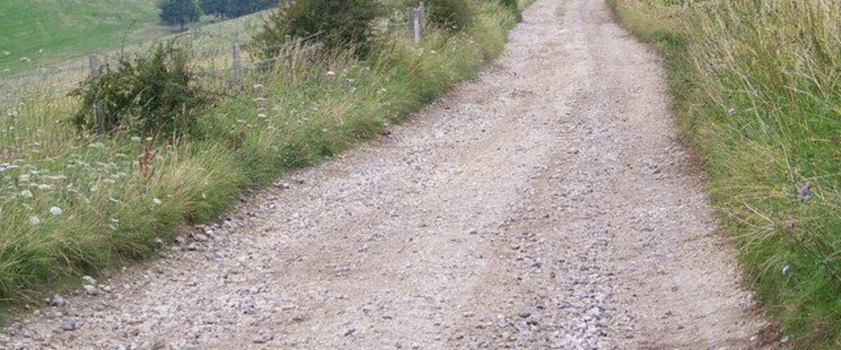 A gravel path leading through a rural landscape with fields, trees, and a small building.