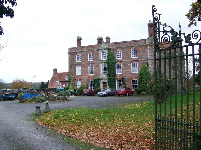 A large brick building with a gated entrance, parked cars, and a grassy area with fallen leaves.